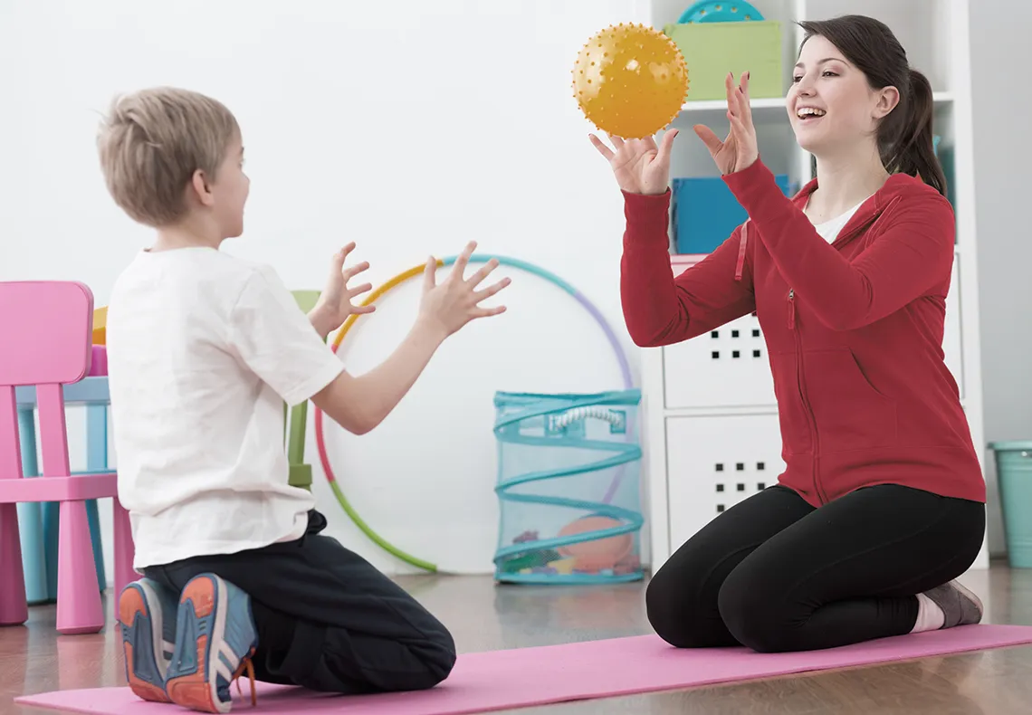 Woman therapist throwing a ball to young boy