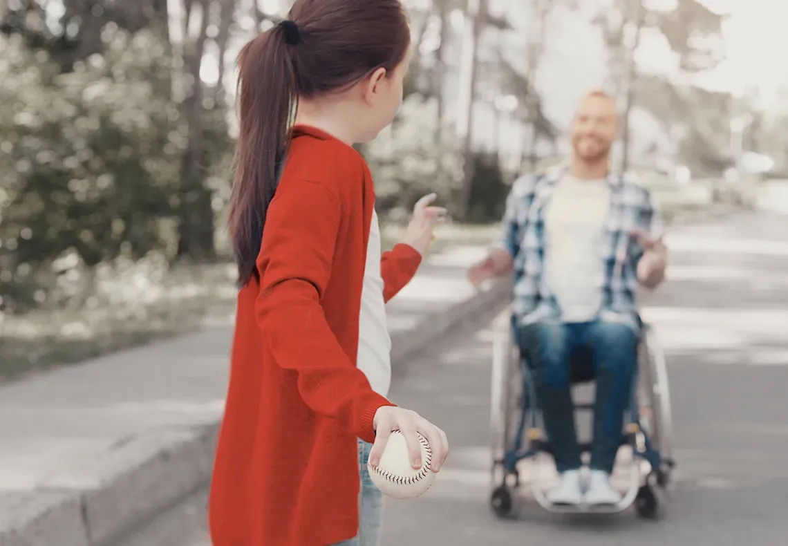 Young girl playing catch with her father who is seated in a wheel chair
